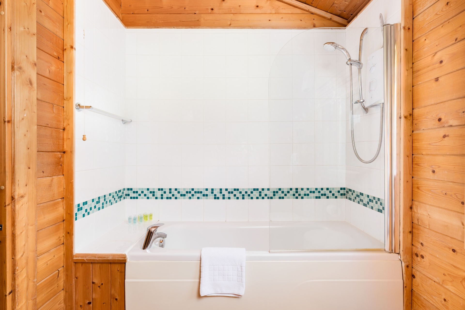 Bath with overhead shower and mosaic tile border at Primrose Lodge