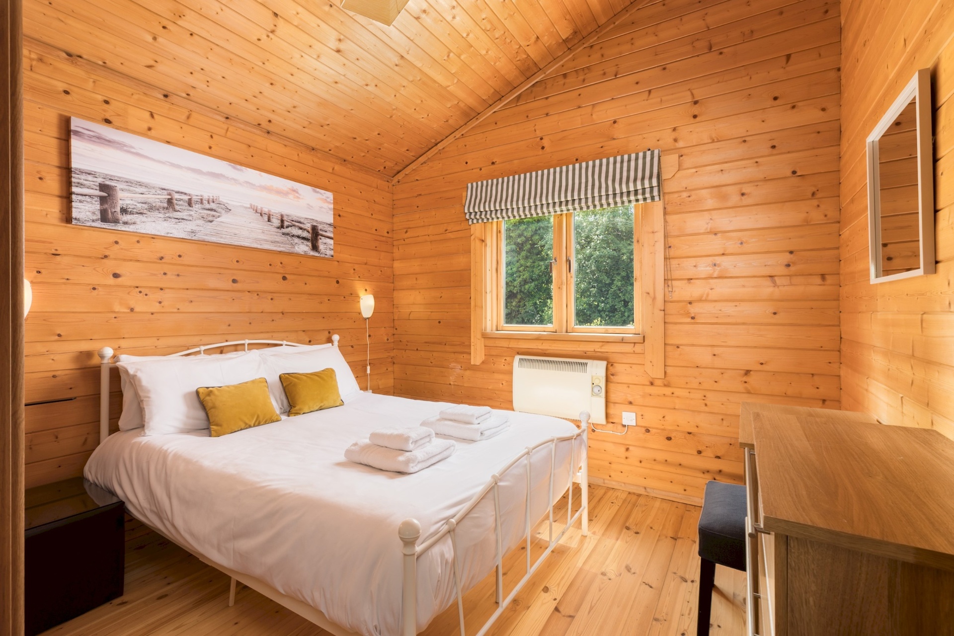 Main bedroom at Primrose Lodge with vaulted pine ceiling and coastal artwork